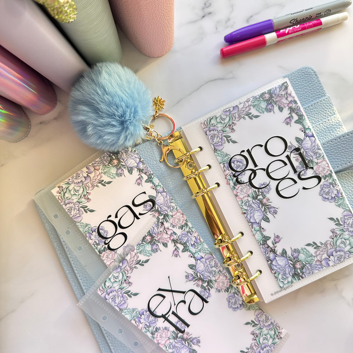Open planner with floral design on a marble surface with stationery items.